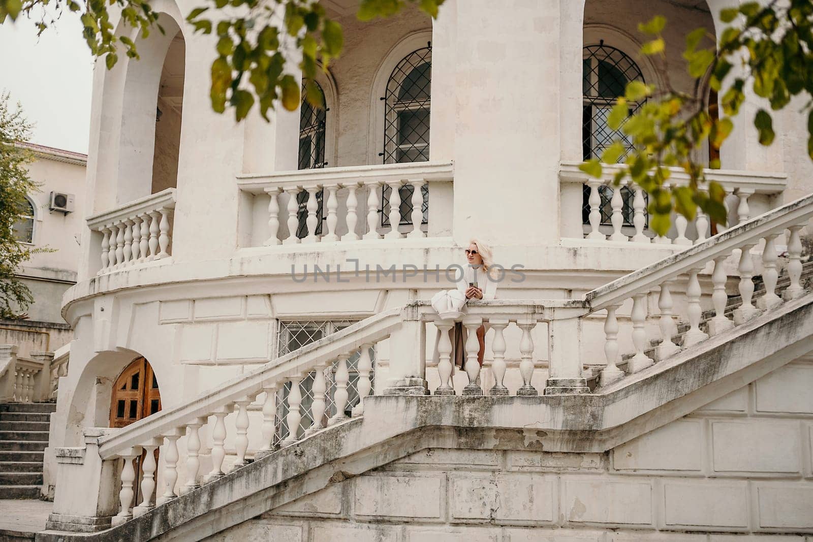 A woman is standing on a balcony of a building with a white hat on. The balcony has a railing and a staircase leading up to it