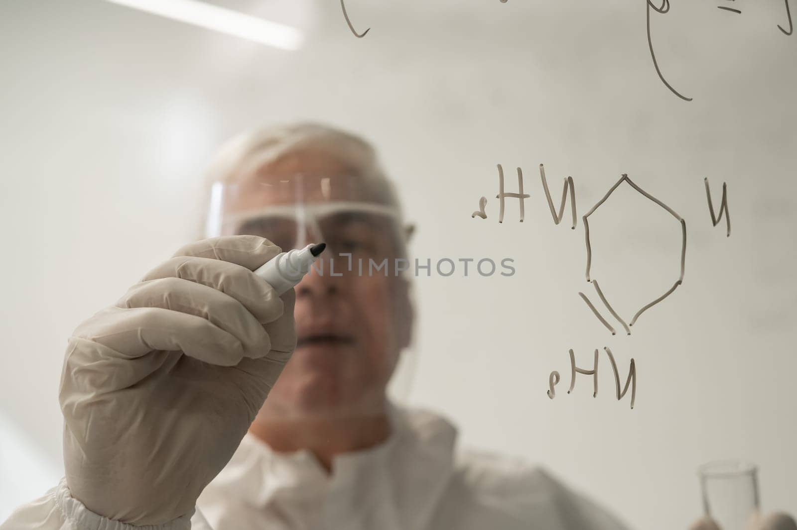 An elderly Caucasian male chemist in a protective suit writes on glass