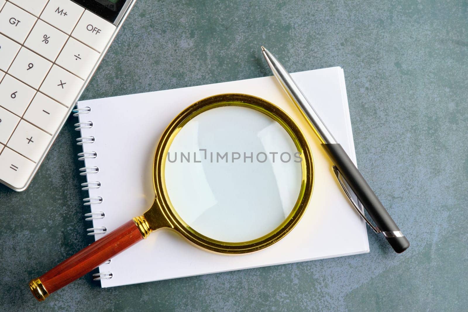 A magnifying glass on top of the notebook next to the calculator and pen. A place to copy