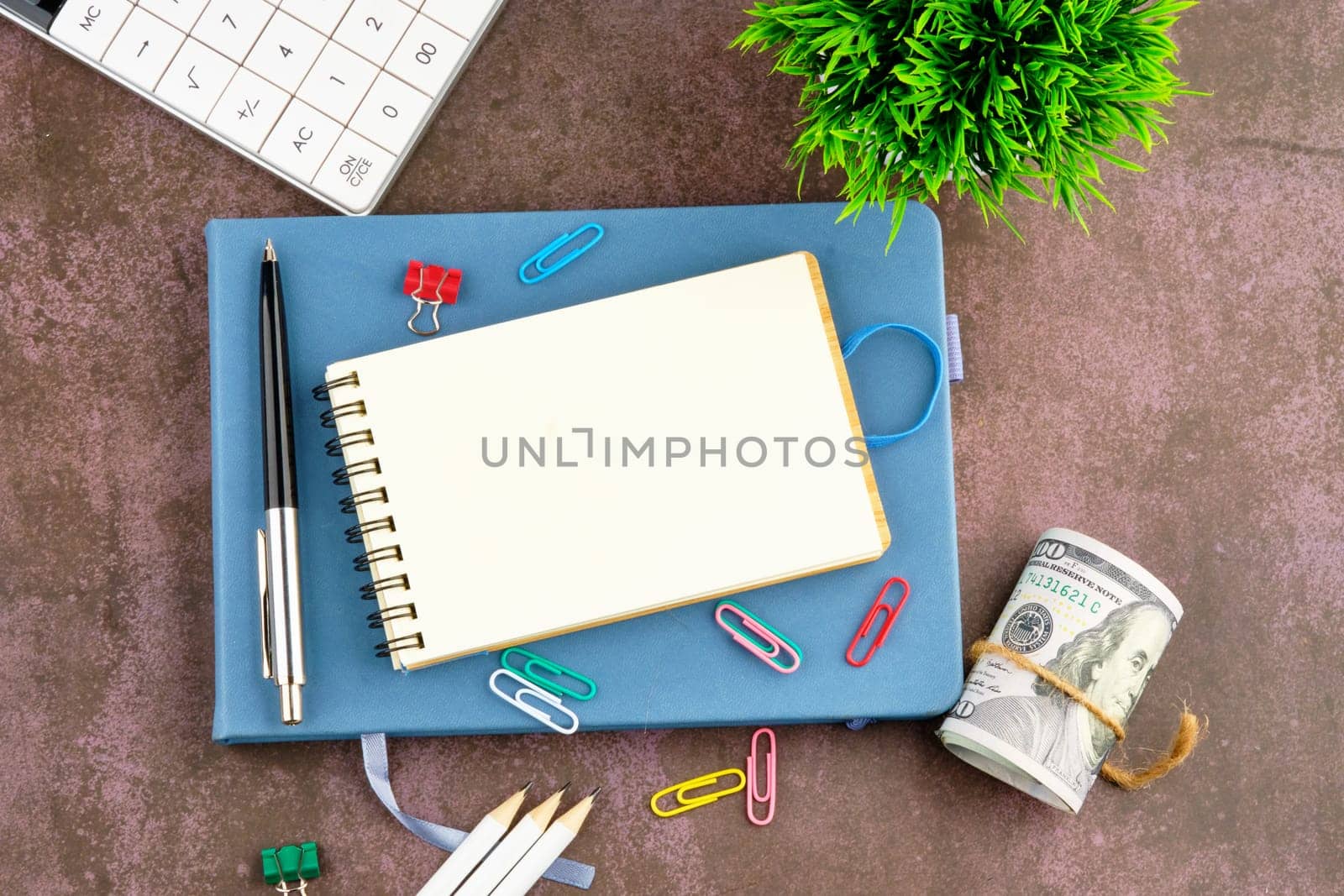 An open notepad for writing next to a pen, paper clips, calculator, pencils and US dollars