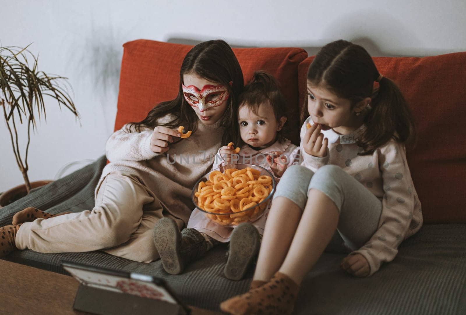 Three girls are watching a movie sitting on the couch. by Nataliya
