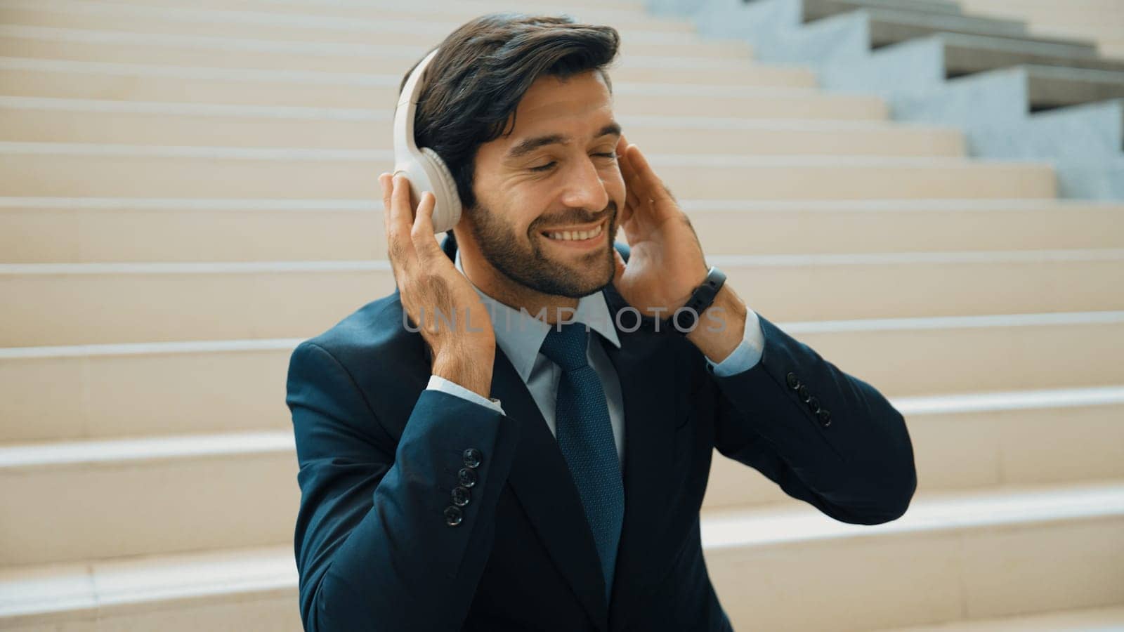 Closeup image of professional business man enjoy to listen music by using headphone. Portrait of skilled project manager show facial expression about joy and happy while sitting at mall. Exultant.