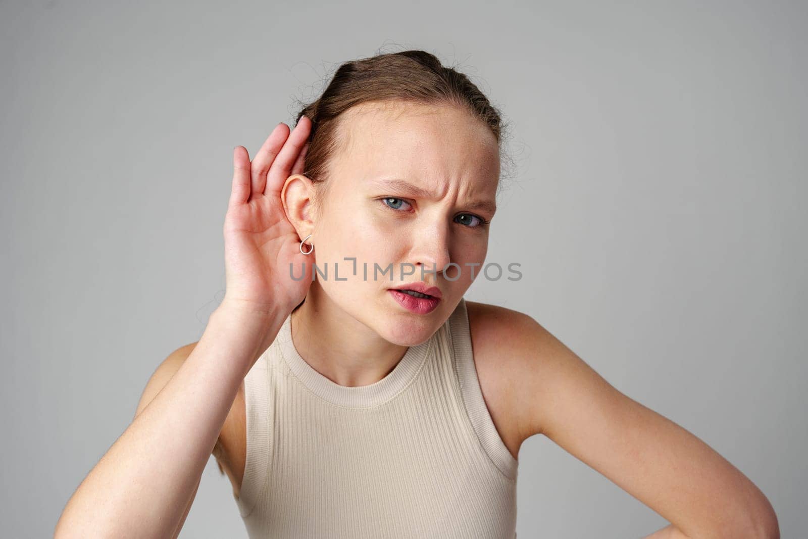 Young Woman Holding Her Ear With Her Hands on gray background in studio