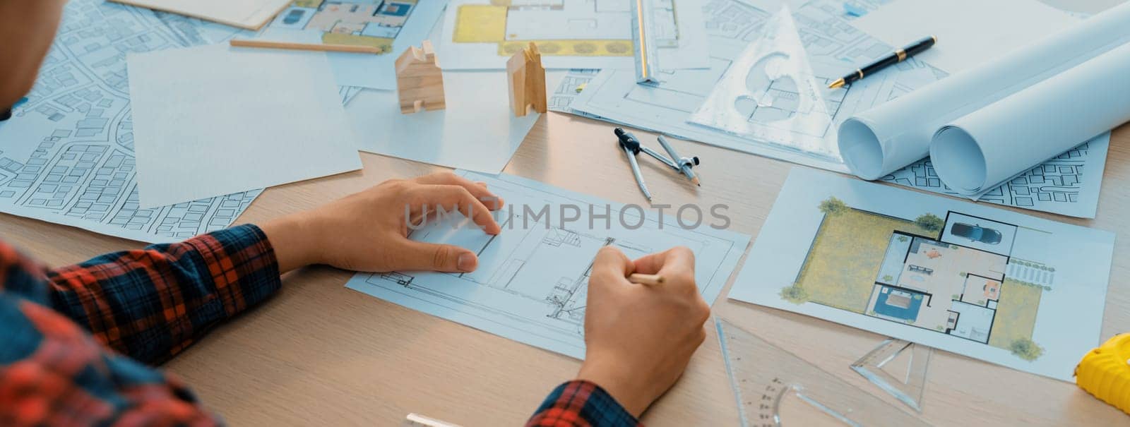 Closeup of architect engineer hand using ruler to mature and draw a blueprint on meeting table with wooden block, pencil and blueprint scatter around at architectural modern office. Delineation.