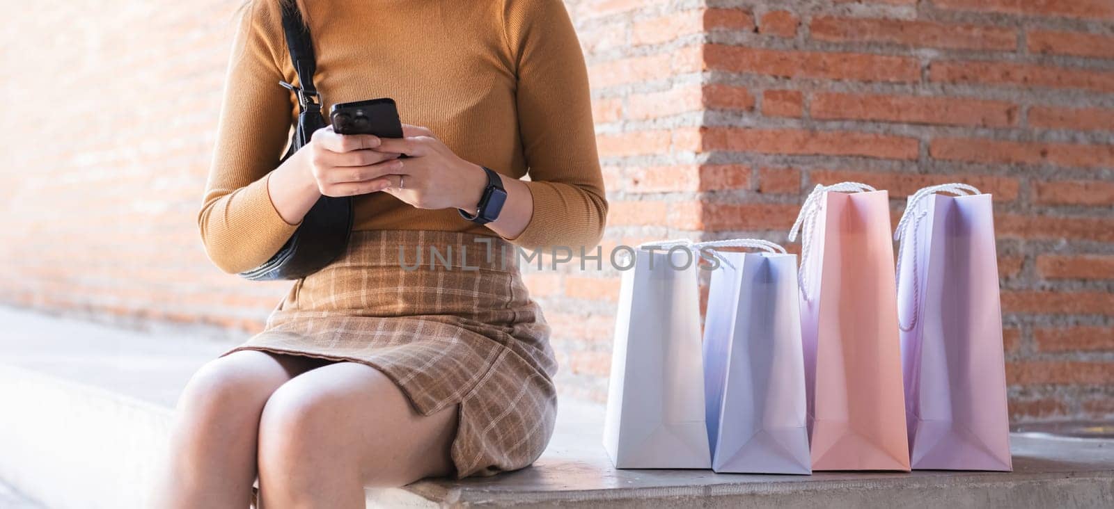 A woman sitting on a bench with a cell phone in her hand and a pink bag in front of her