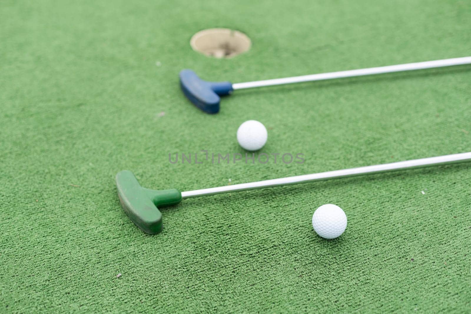 Mini-golf clubs and balls of different colors laid on artificial grass. High quality photo