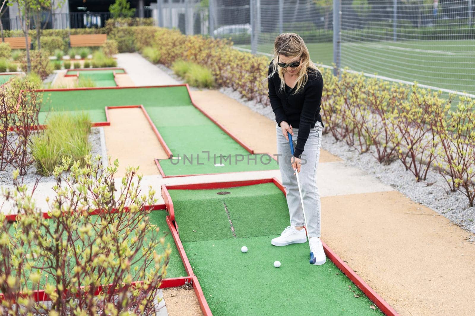 Woman playing mini golf and trying putting ball into hole. Summer leisure activity by Andelov13