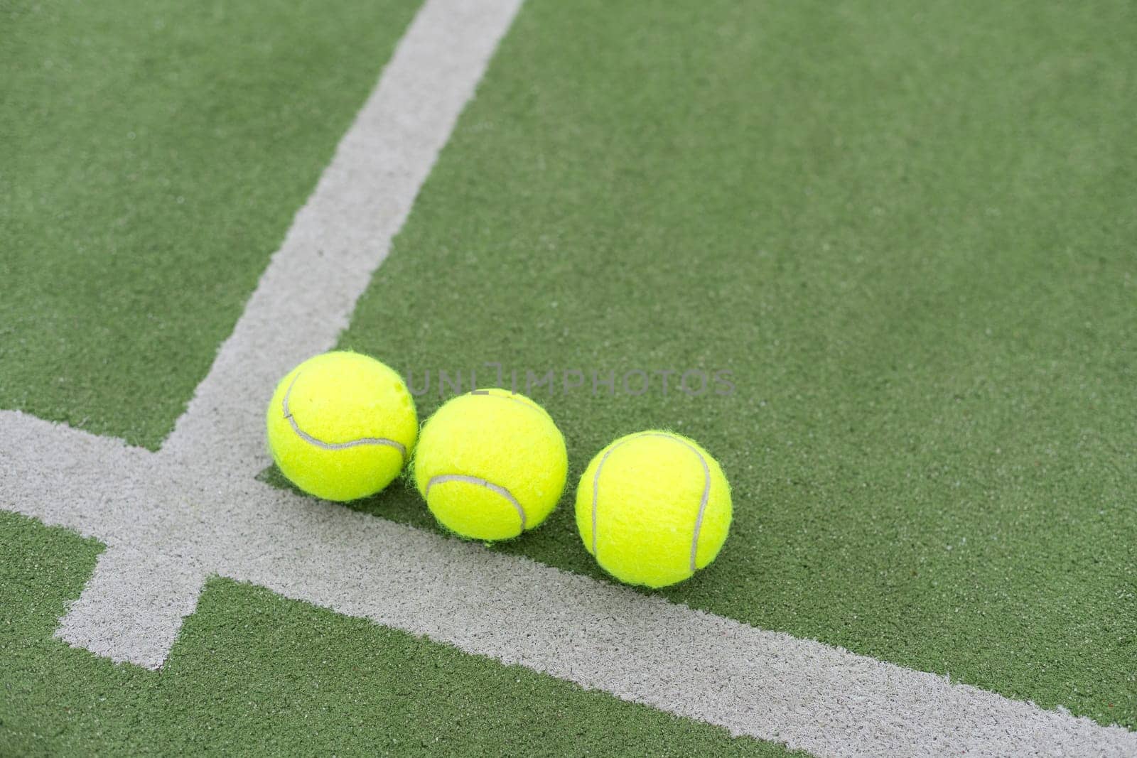 Yellow balls on grass turf near padel tennis racket behind net in green court outdoors with natural lighting. Paddle is a racquet game. Professional sport concept with copy space. High quality photo
