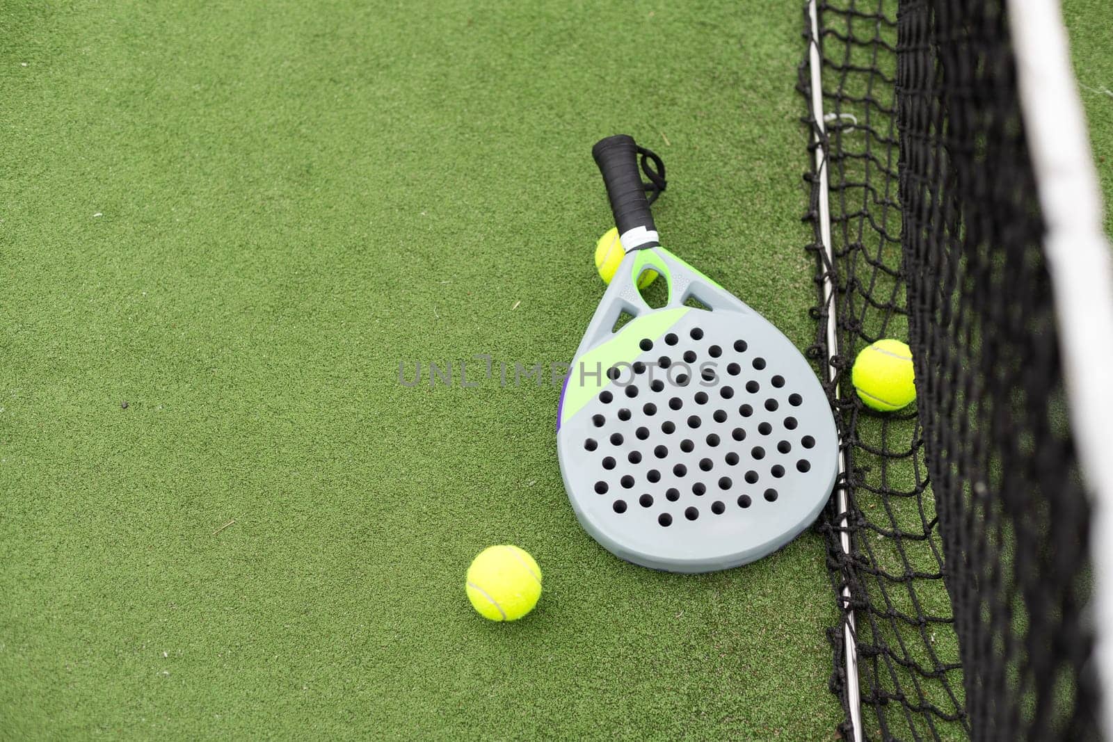 Closeup view of a paddle racket and balls in a padel tennis court near the net. Green background with white lines. Sport, health, youth and leisure concept. Sporty equipment. High quality photo