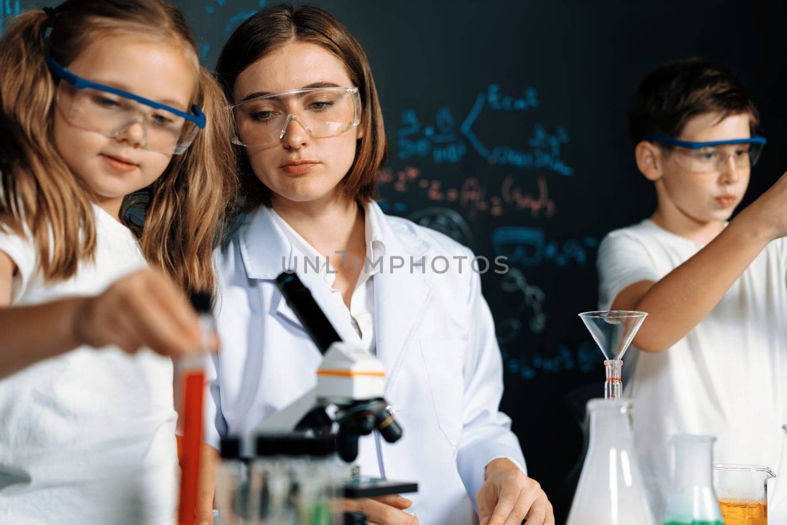 Teacher in support and watch student in laboratory they wear safety glasses, stand and experiment about science of chemistry in STEM class. Student funny do experiment with liquid in tube. Erudition.