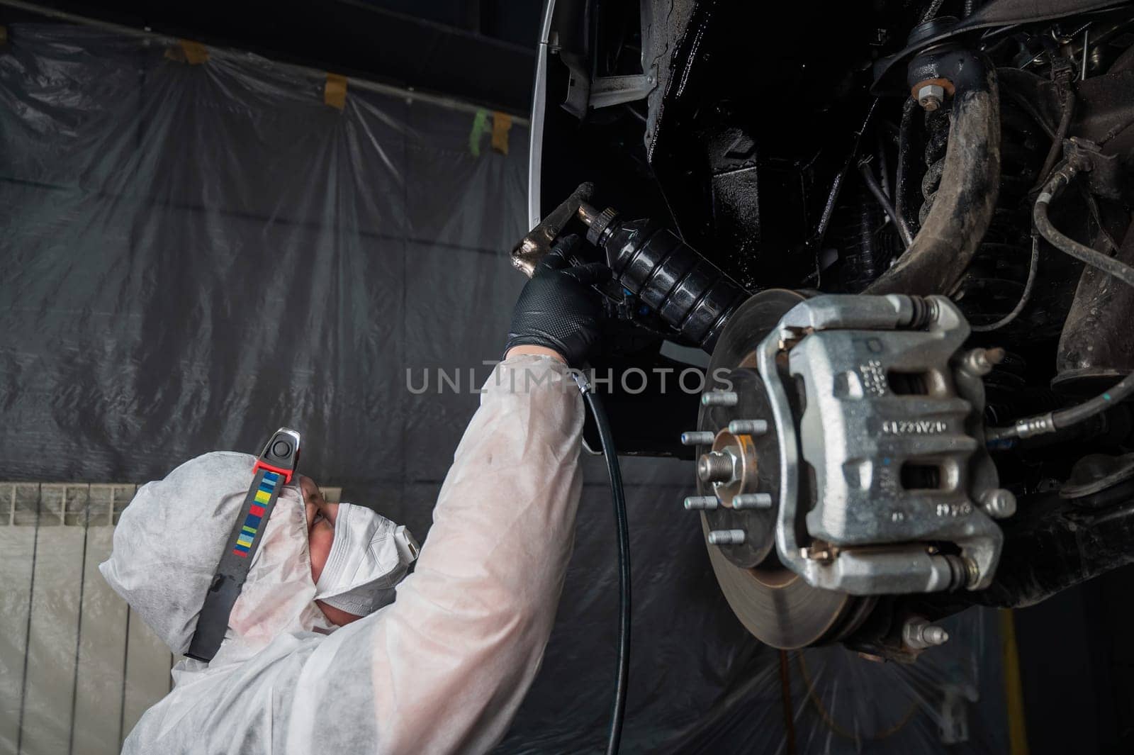 An auto mechanic applies anti-corrosion mastic to the underbody of a car. by mrwed54