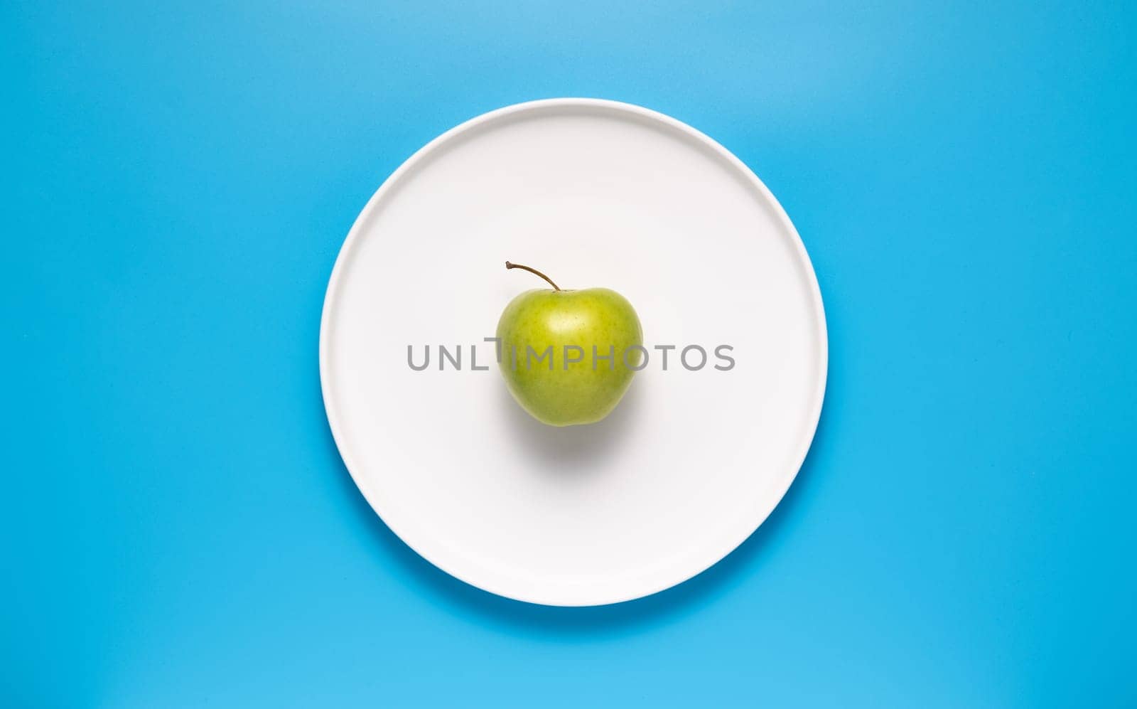 Fresh green apple on a white plate on a blue background.