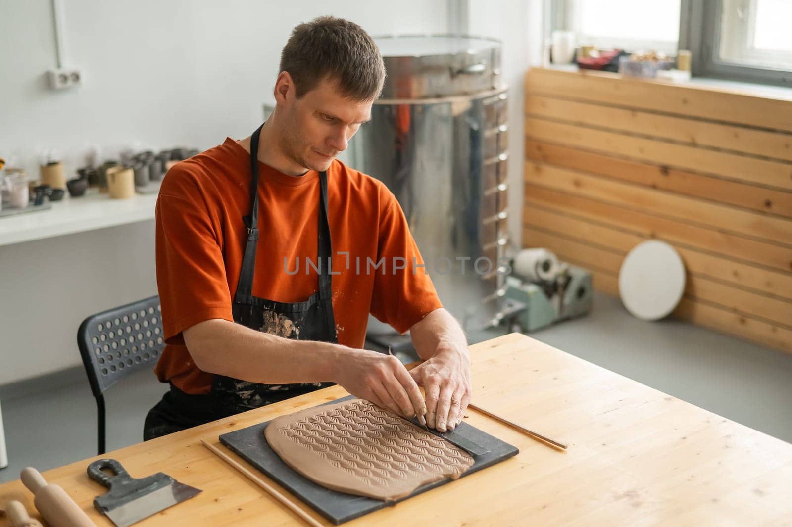 A potter cuts a piece of rolled clay with patterns. by mrwed54