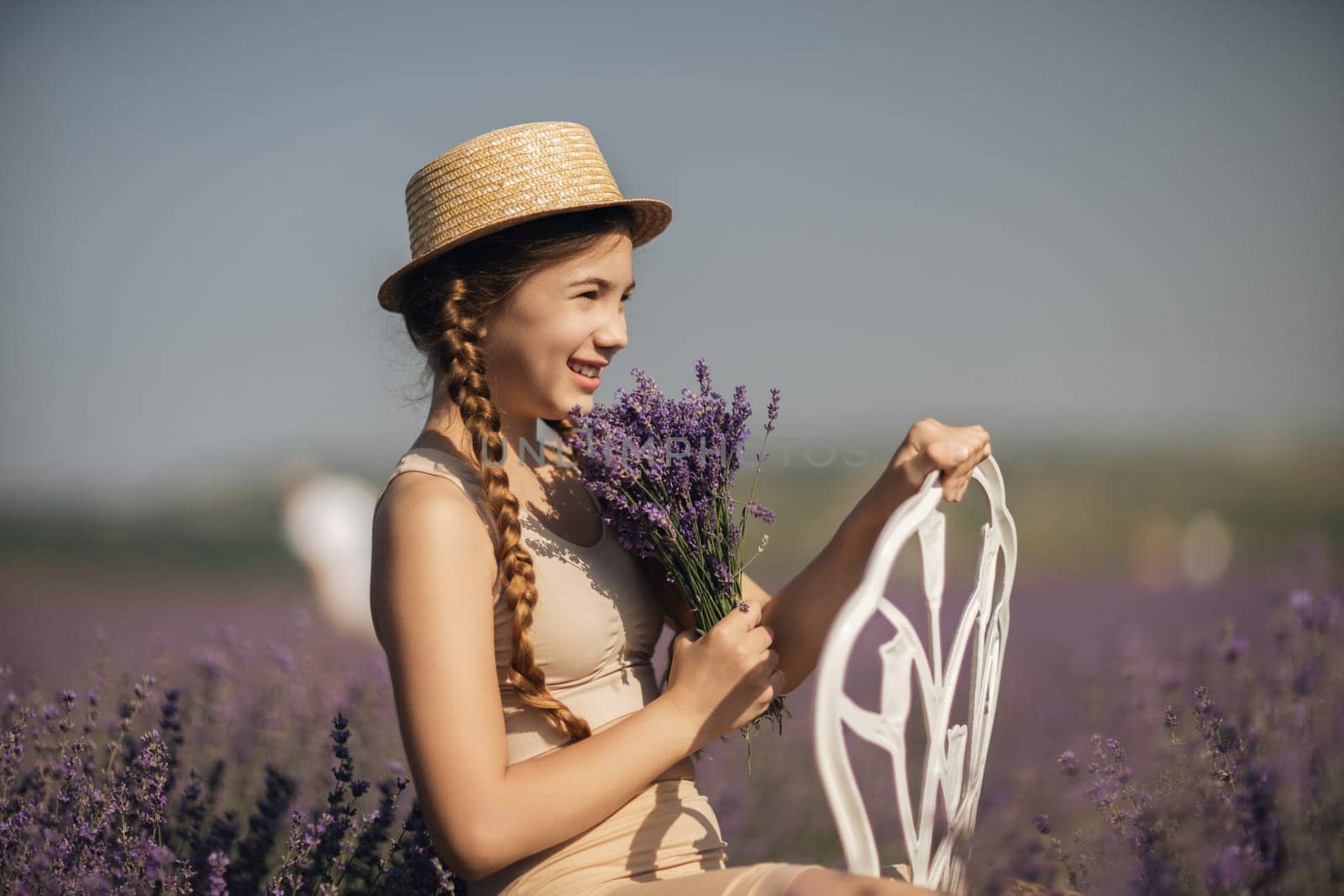 girl sitting field lavender and wearing a straw hat. She is smiling and holding a bouquet of flowers.