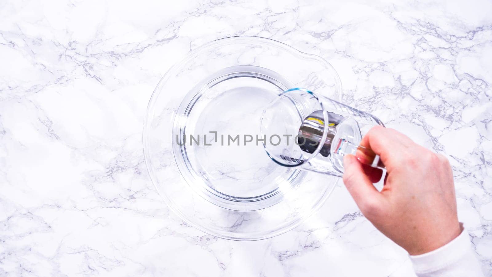 Flat lay. A spacious glass mixing bowl filled with water sits prepared to gently cleanse a batch of ripe strawberries, ensuring they are pristine before drying or storage.