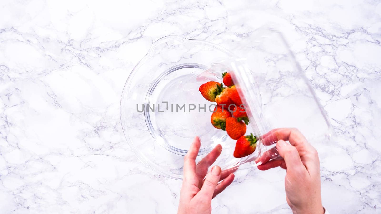 Flat lay. Ripe strawberries are submerged in water within a large glass mixing bowl, a step in washing the fruit to ensure cleanliness and longevity before storage or consumption.
