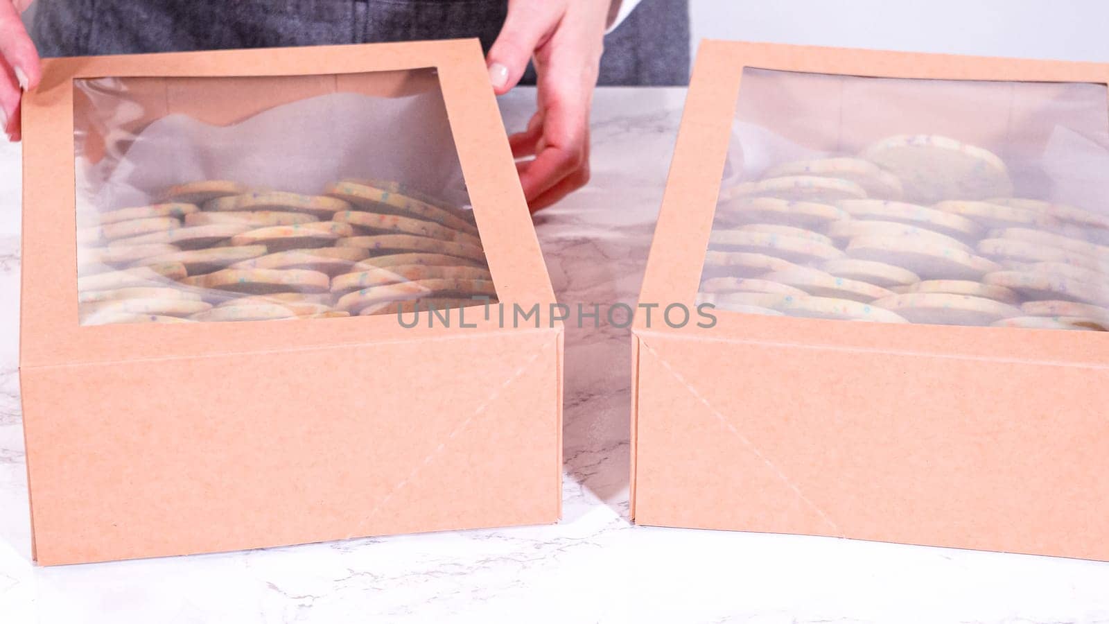 The sugar cookies, filled with sprinkles mixed into the dough, are carefully arranged with meticulous precision into a rustic brown paper box.