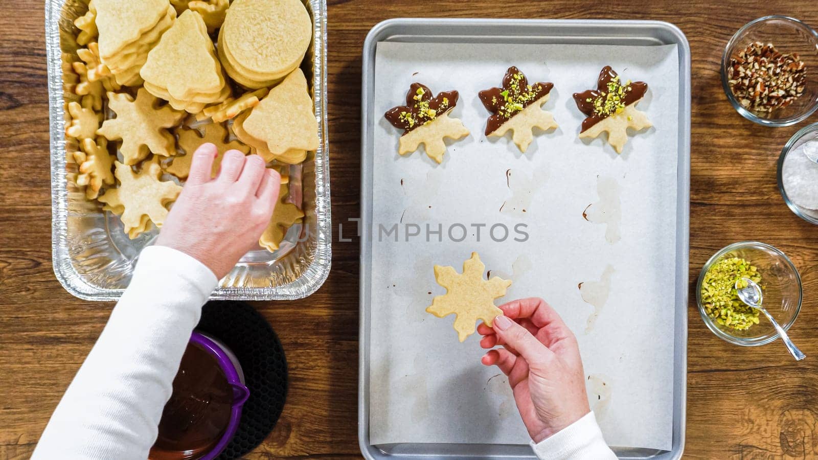 Flat lay. Creating snowflake-shaped cutout sugar cookies, dipped in chocolate, and adorned with different toppings.