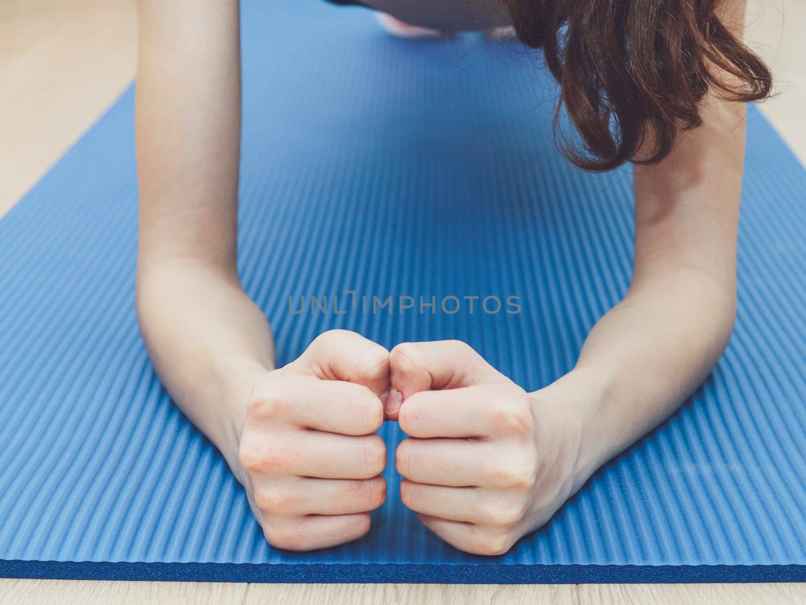 A young caucasian girl teenager without a face does a plank exercise on a blue mat. by Nataliya