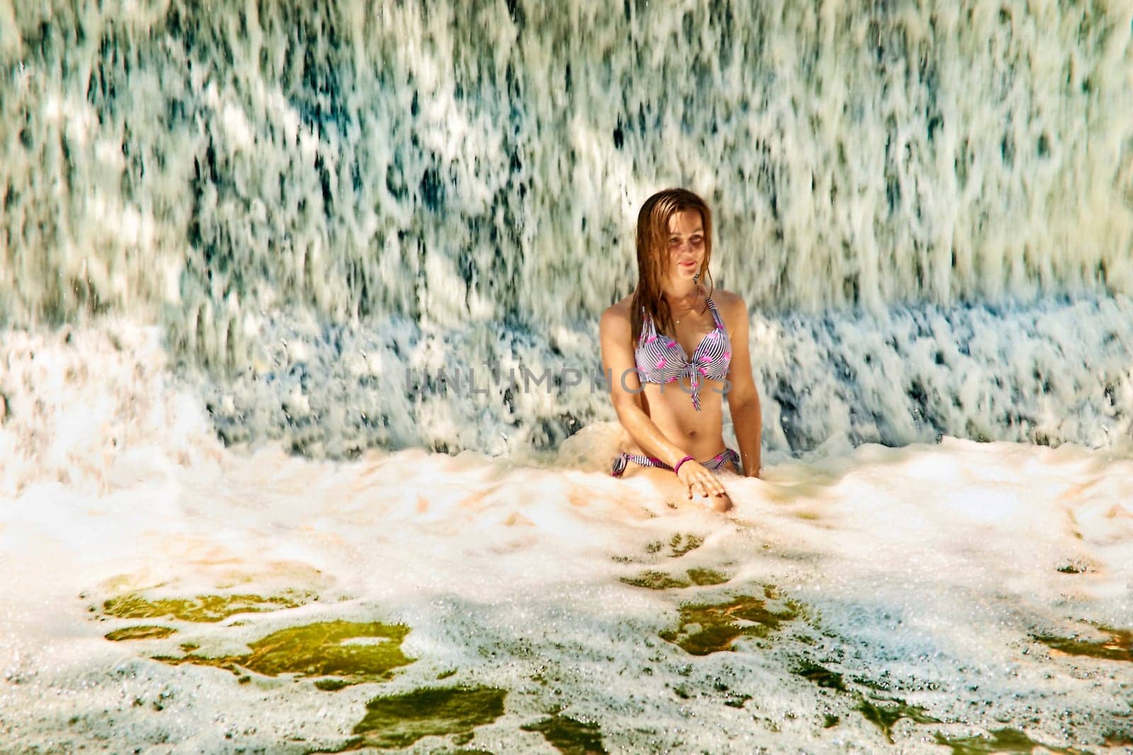 Pretty girls enjoying stream of waterfall in swimming pool at spa resort by jovani68