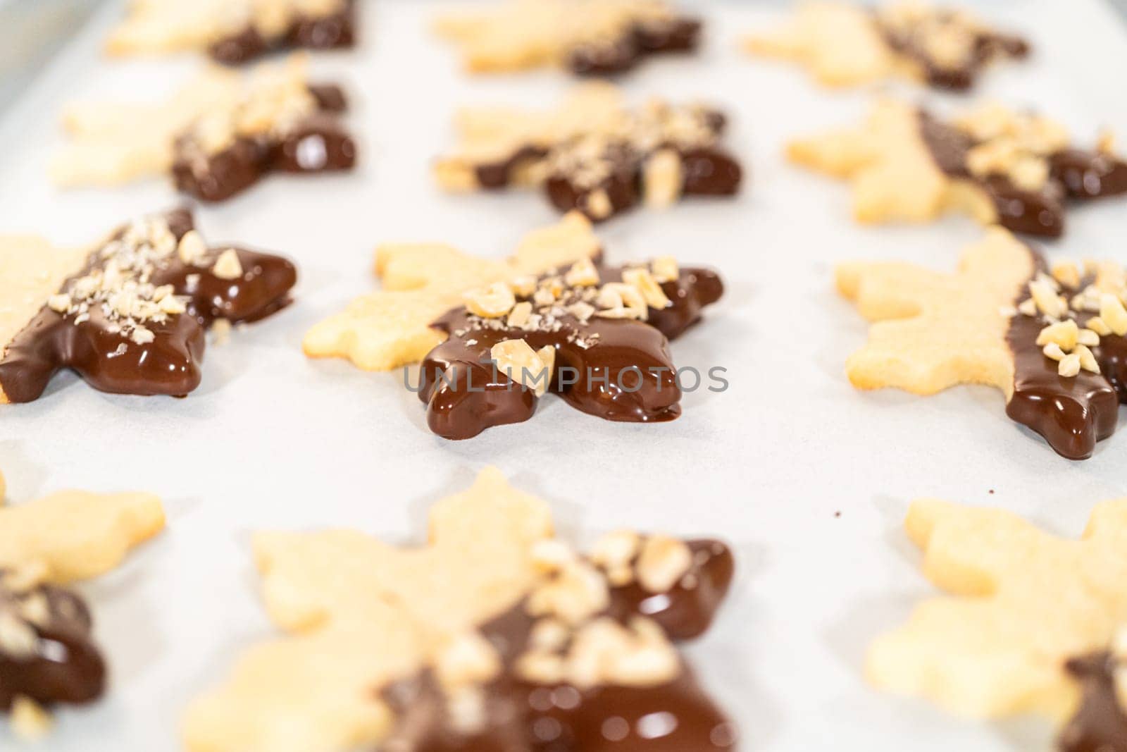 Creating cutout sugar cookies, partially dipped in chocolate and topped with hazelnut pieces, placed on parchment paper.