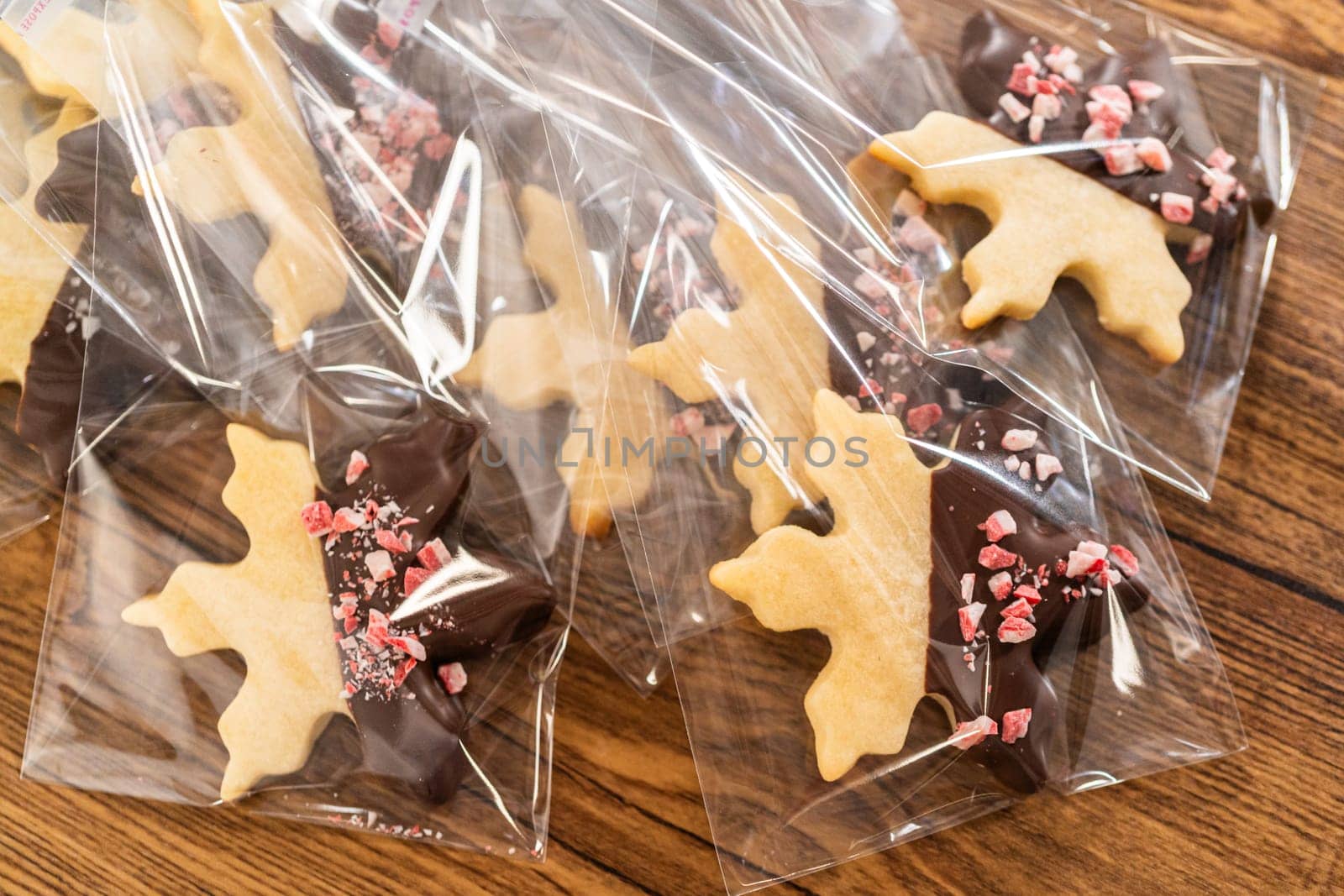 Carefully packaging Christmas cutout cookies, half-dipped in chocolate and presented in clear cellophane wrapping, perfect for festive gifting.