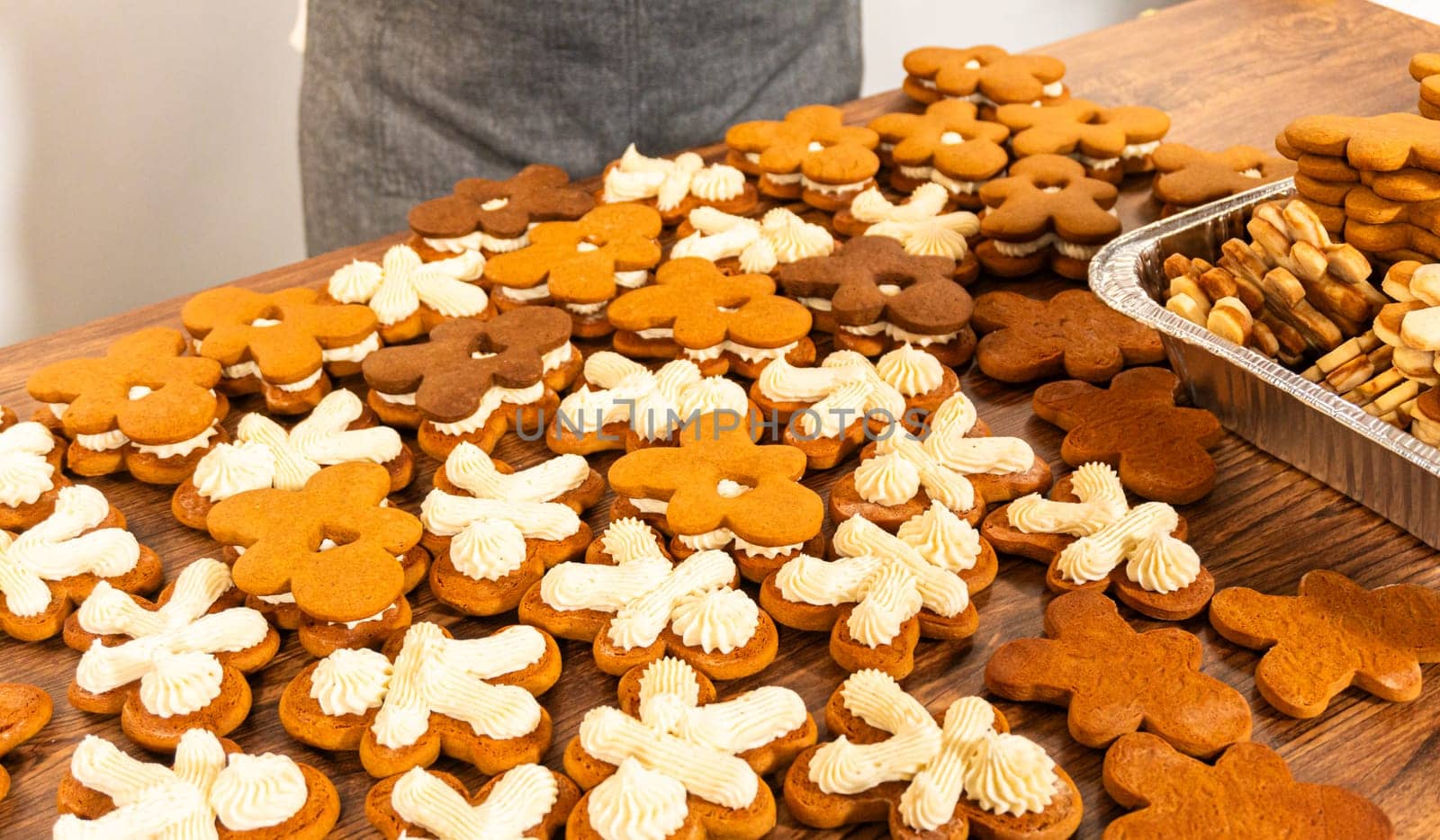 Making gingerbread man cookie sandwiches filled with eggnog buttercream, arrayed on a rustic wooden table, ideal for heartfelt Christmas gifting.