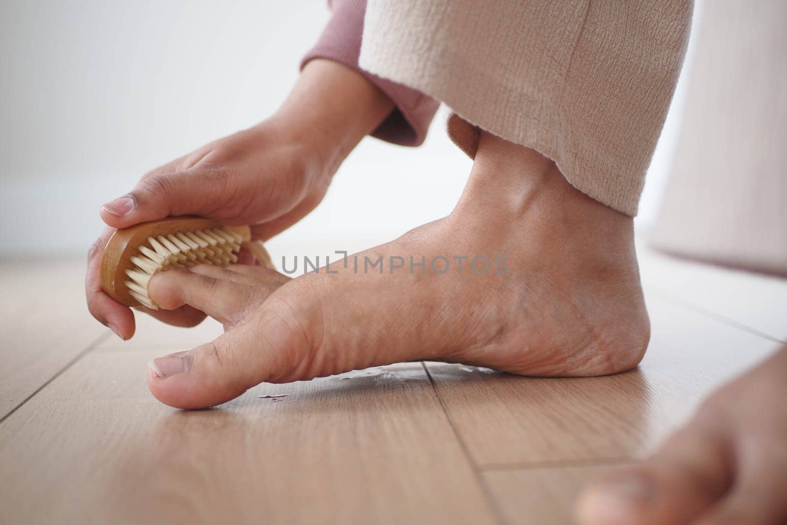 Using a brush, the person gently brushes their foot on the hardwood flooring.