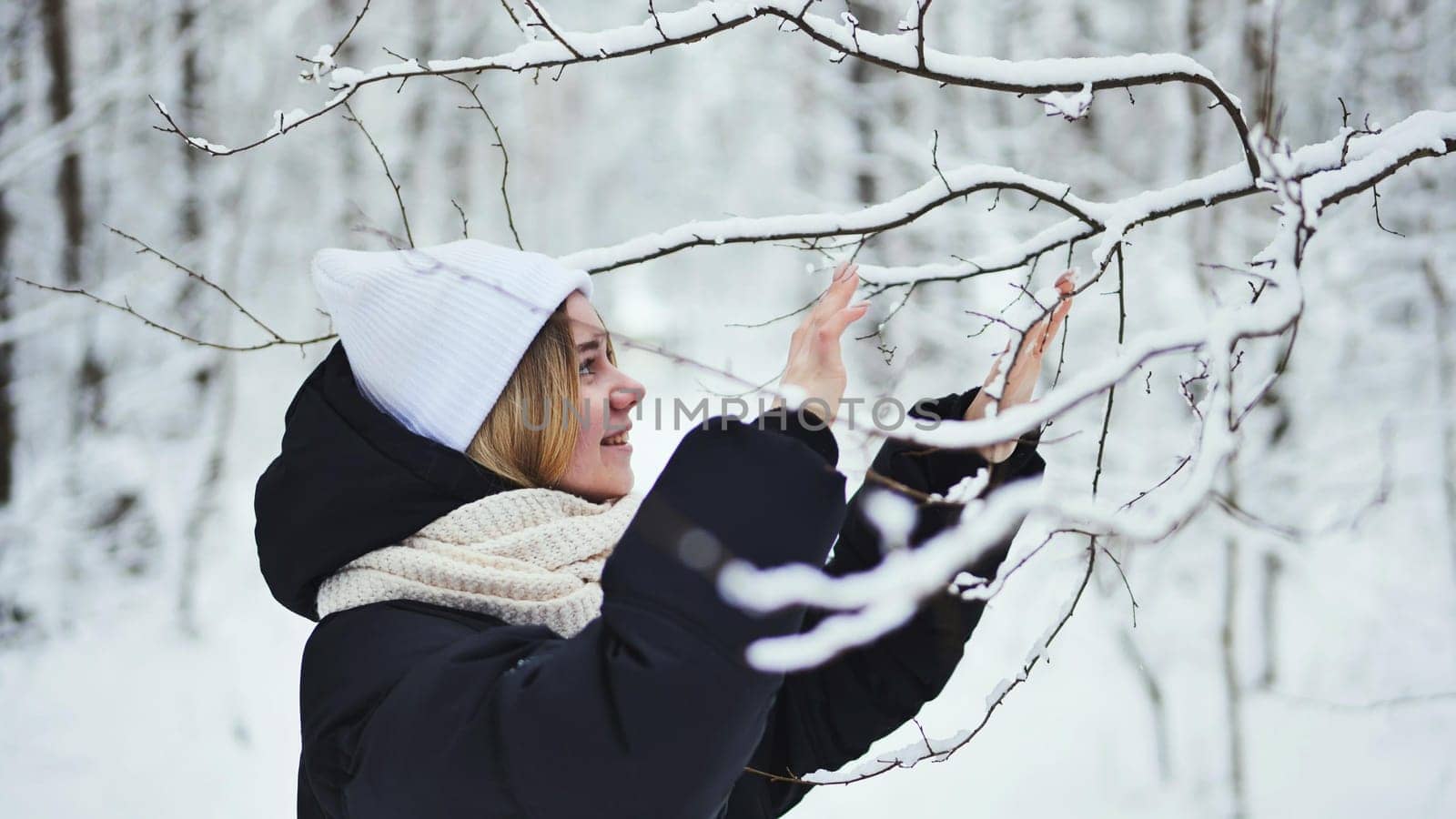 A girl gently touches snowy tree branches in the forest. by DovidPro