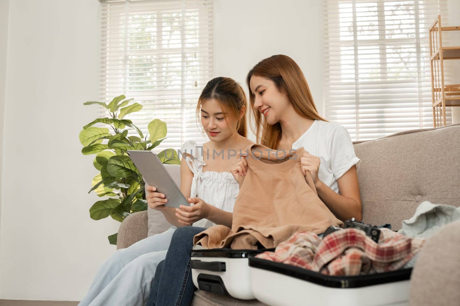 Two young female friends use a tablet to view travel information online for a vacation together. While packing your suitcase.