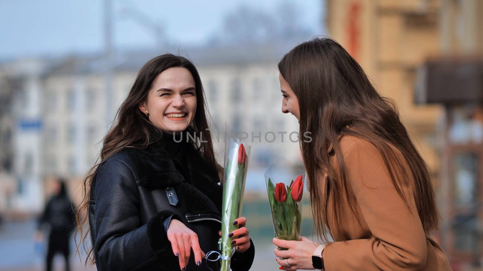 two happy girls, students, friends with flowers in their hands, laughing by DovidPro