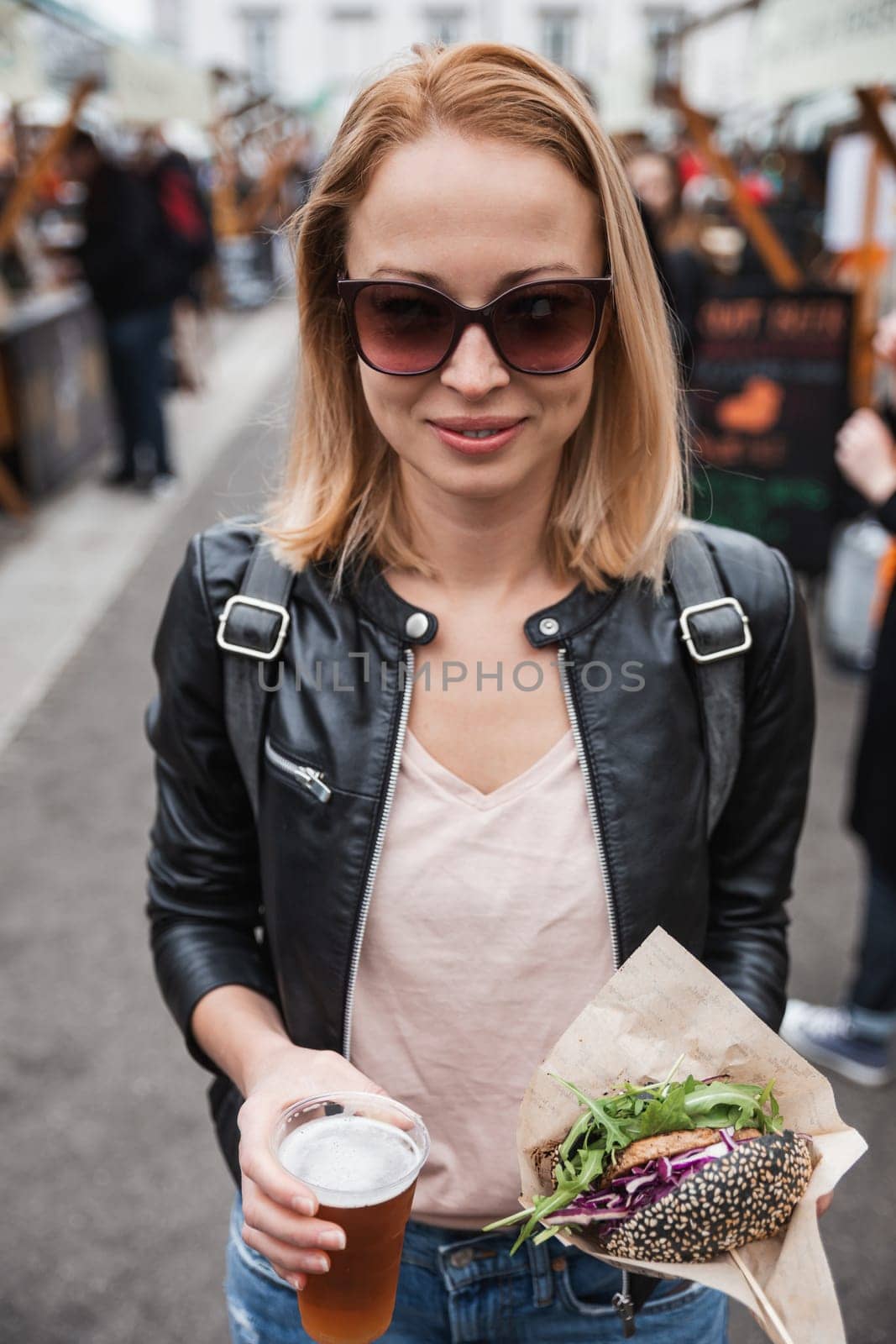 Beautiful young woman holding delicious organic salmon vegetarian burger and homebrewed IPA beer on open air beer an burger urban street food festival in Ljubljana, Slovenia