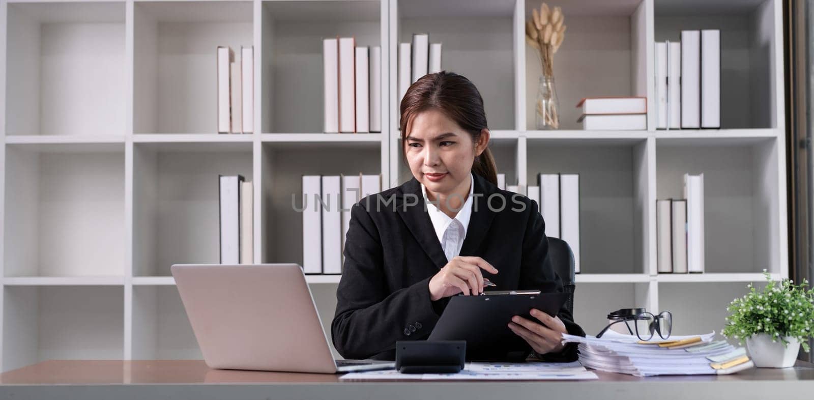 Young business woman meeting on laptop, doing paperwork in white office room.