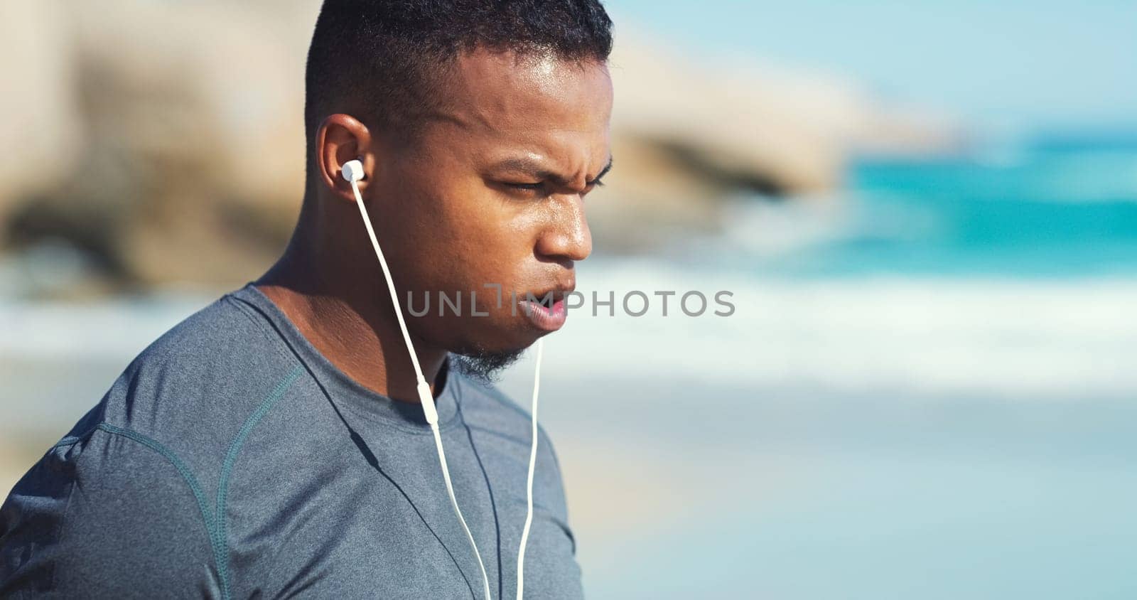 Fitness, headphones and black man with fatigue at beach to relax on audio, streaming and training. Workout, music and tired runner at ocean, listening to podcast and exercise challenge in nature.