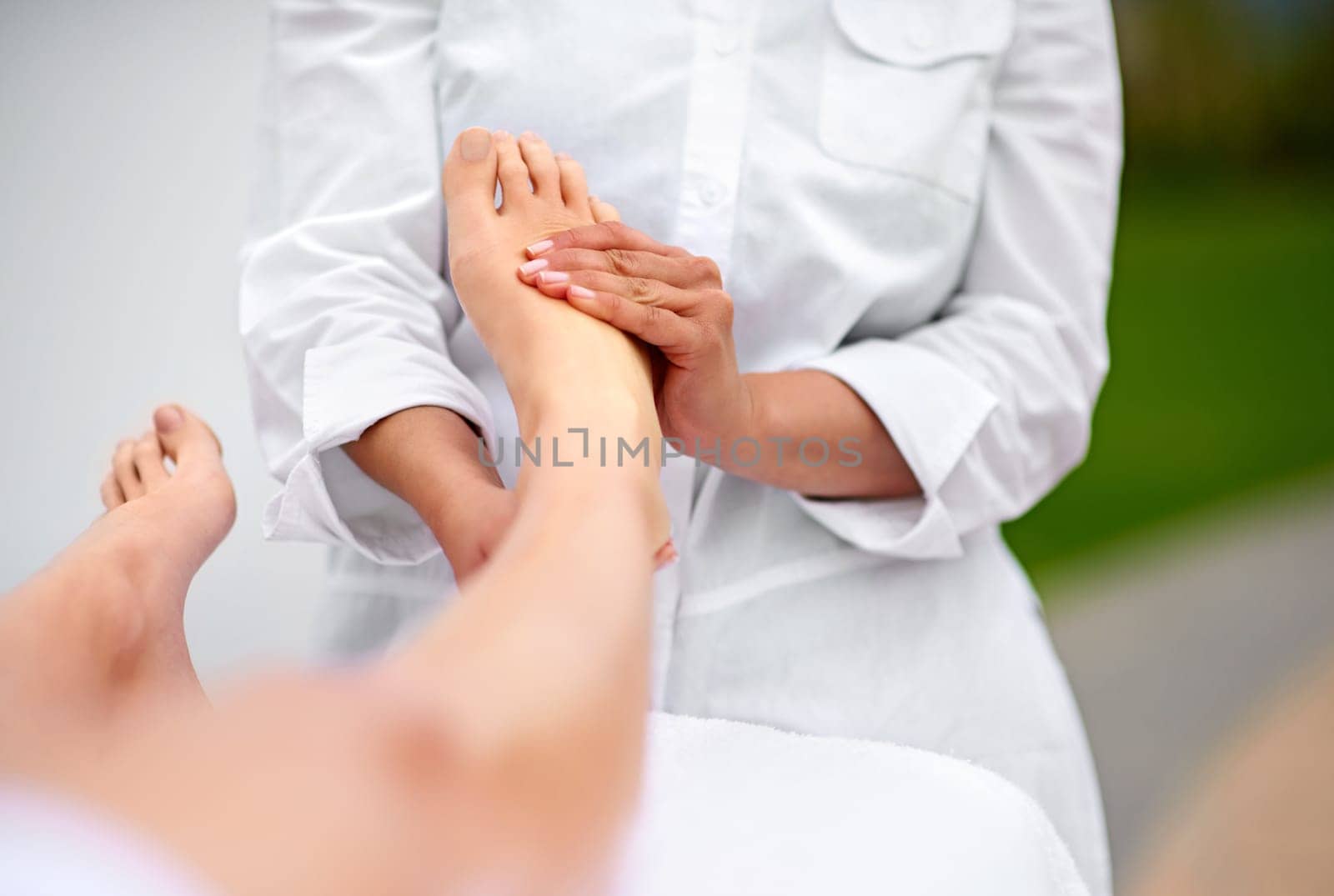 Woman, relax and foot for massage at spa from therapist for treatment or pedicure with hands for health or skincare. Professional, therapy and zen with body care or healing for wellness at resort by YuriArcurs