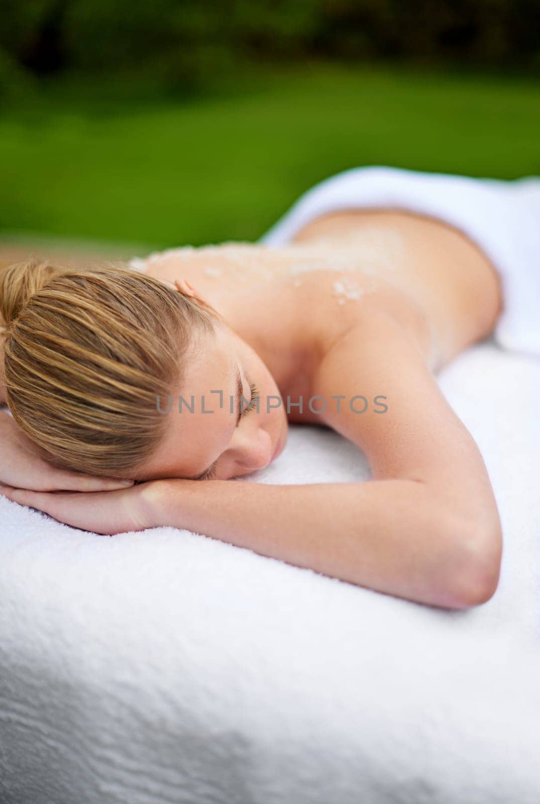 Woman, relaxing and table in spa with salt, therapy and self care for body wellness and resting for tension. Comfortable and resort and client, treatment and healing, exfoliate session or cosmetology.