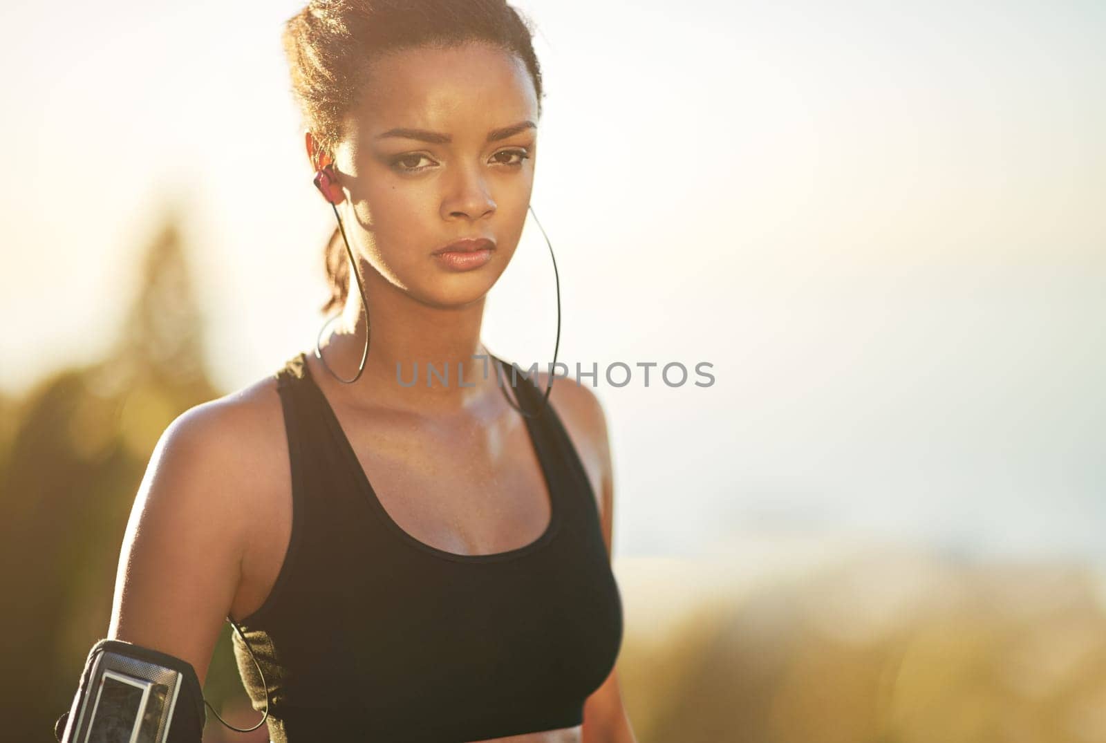 Portrait, girl and running with outdoor, cardio and blurred background for endurance, training and exercise. Athletic, health and work out with arm pouch, earphones and fitness listening to music.