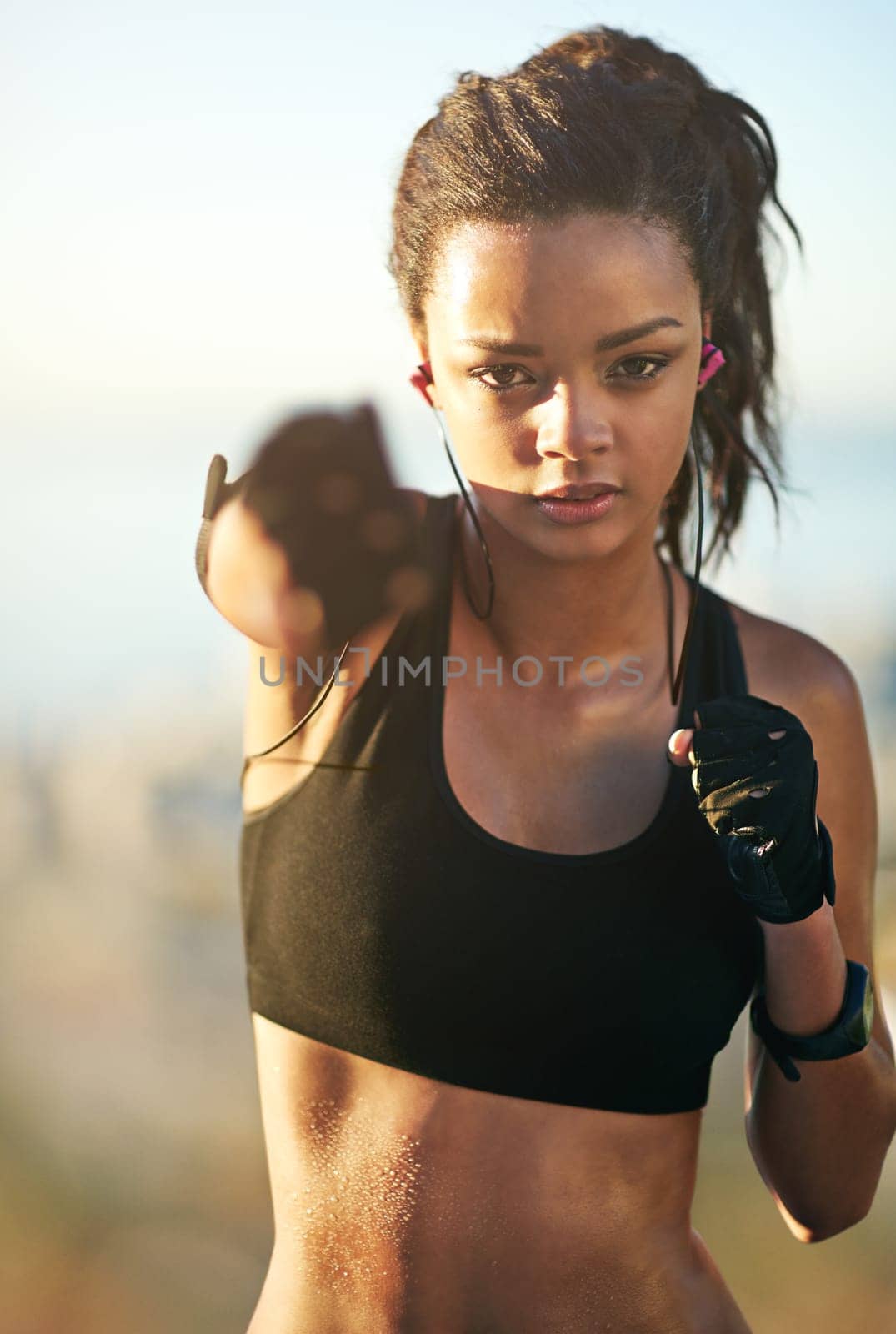 Woman, portrait and fist punch for boxing workout in nature park with earphones for music, listening or confidence. Female person, face and hands for fighter practice with radio, playlist or audio.