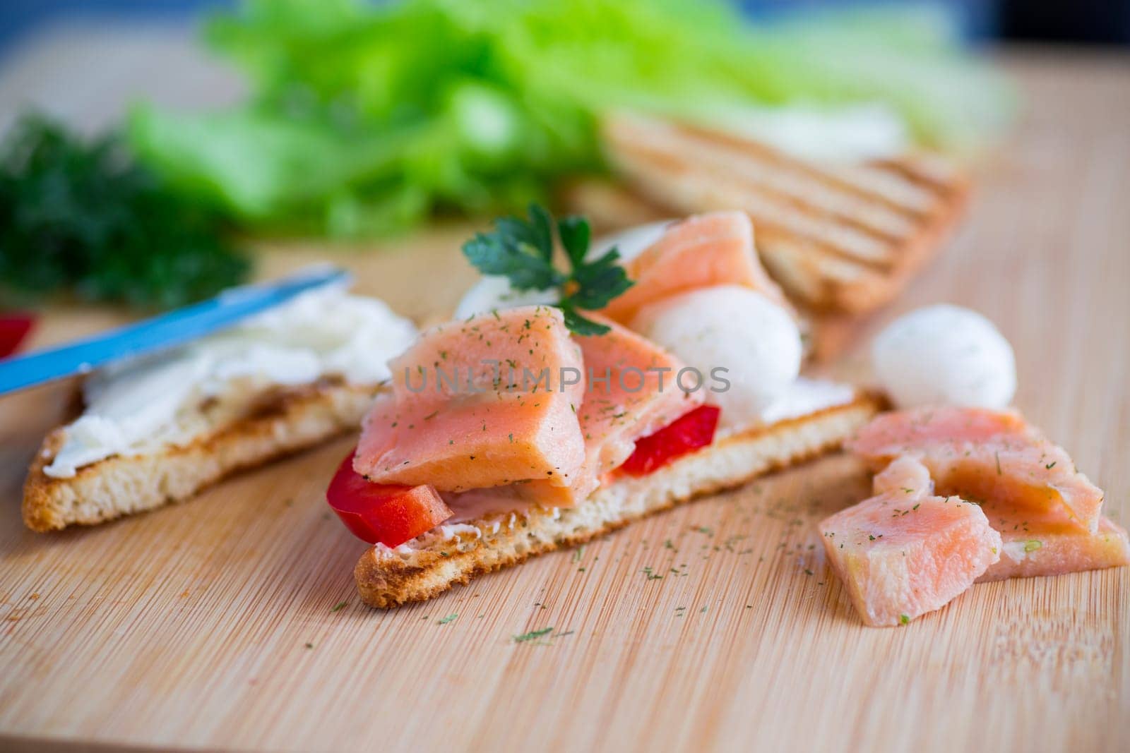 fried toast with salmon, cream cheese, salad, on a wooden table .