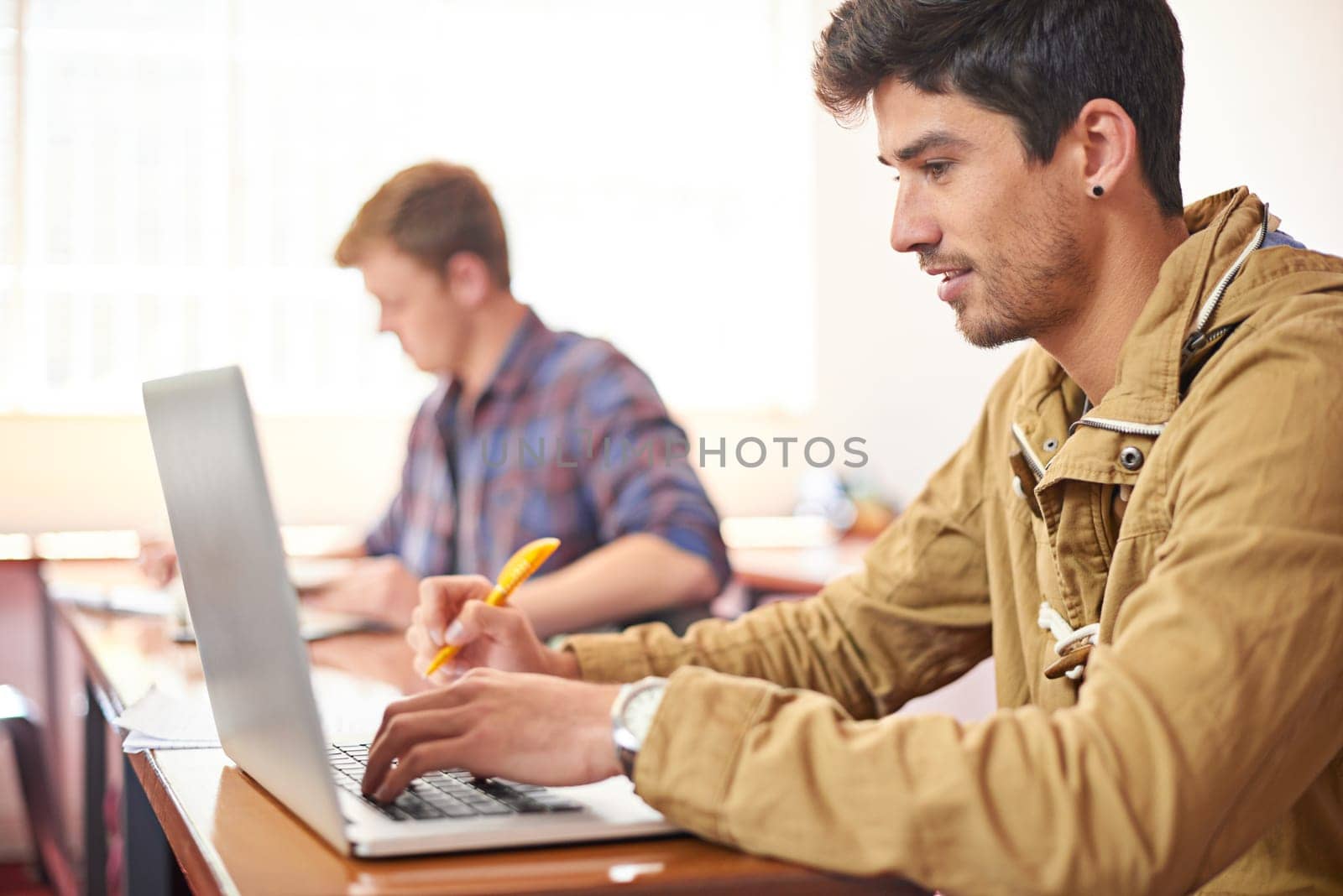 College student, man and laptop with typing in classroom for studying, research or assessment for development. Person, education and learning on computer to search for academic article at university.