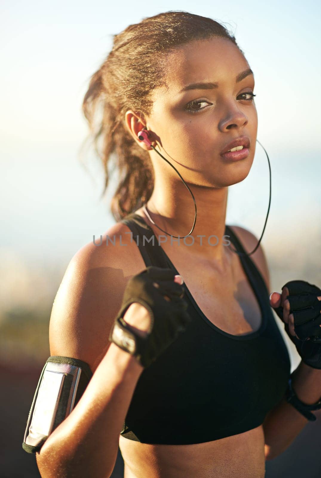 Woman, portrait and outdoor exercise as boxer with fists or earphones or cellphone arm strap, fitness app or fighter. Female person, face and music listening for outside cardio, nature or training by YuriArcurs