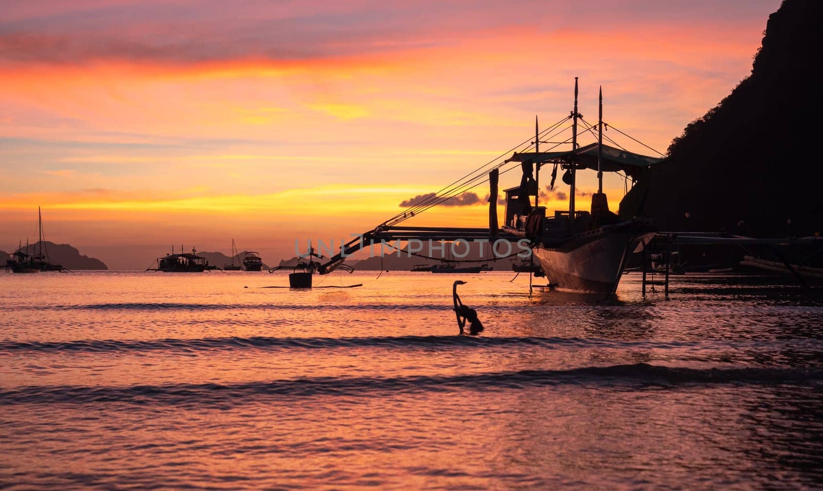 Traditional philippine boat bangka at sunset time. Beautiful sunset with silhouettes of philippine boats in El Nido, Palawan island, Philippines. Orange sky sunset paradise beach. by Busker