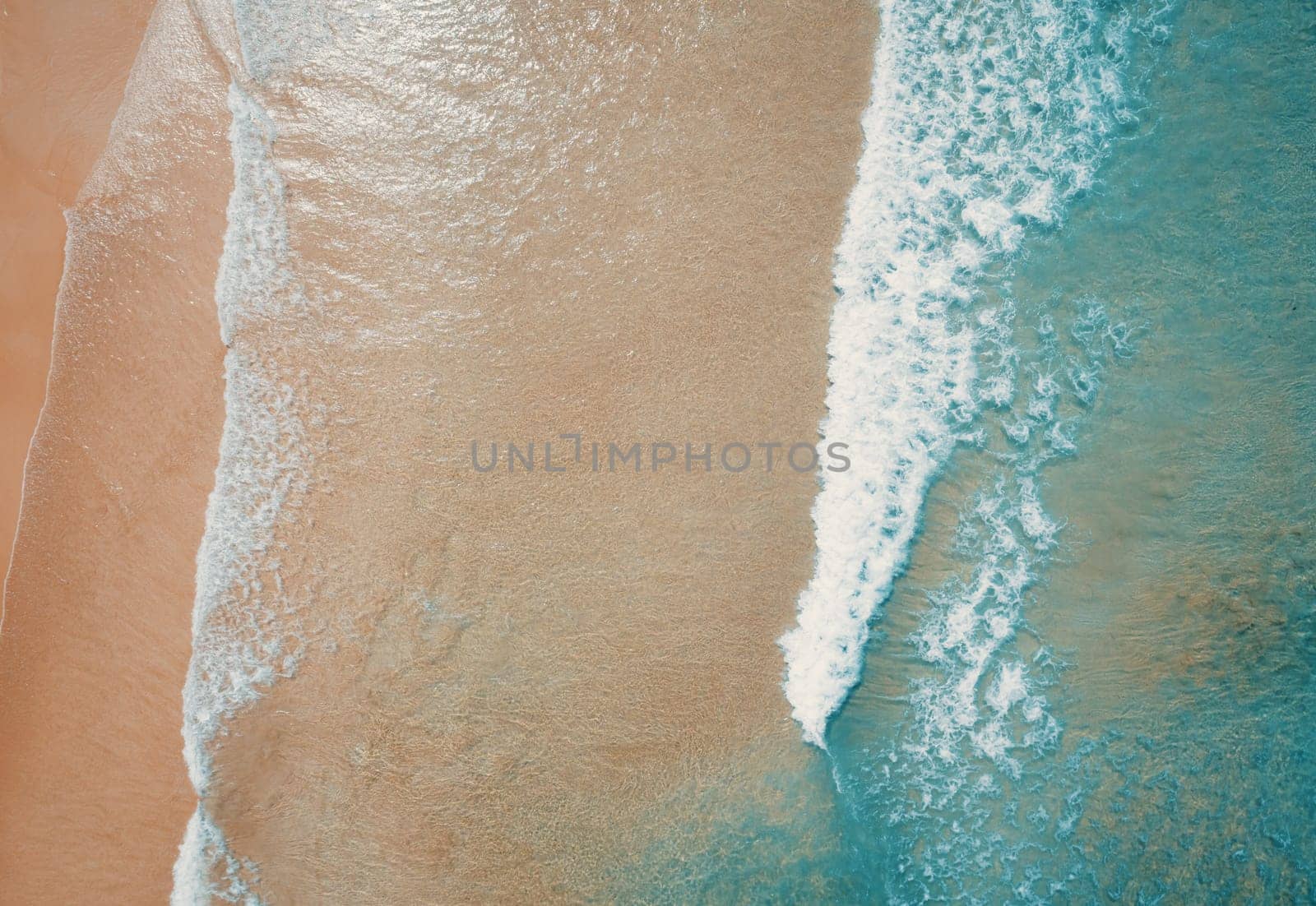 Aerial top view of turquoise ocean wave reaching the coastline.