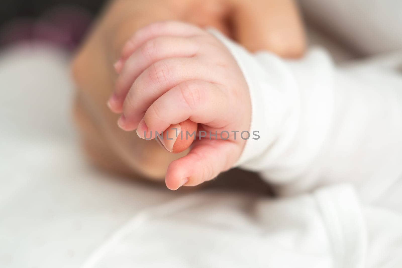 Close-up of a dreaming newborn baby, tightly holding mother's hand, communicates pure love and trust