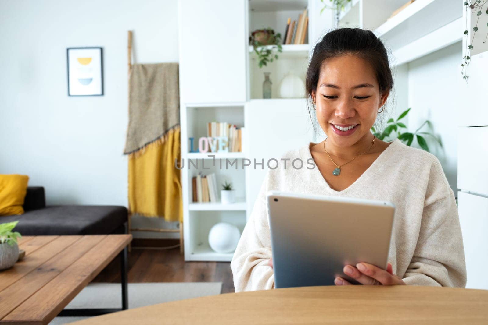 Happy and smiling young Asian woman working at home office holding tablet reading document. Social media. Technology concept.