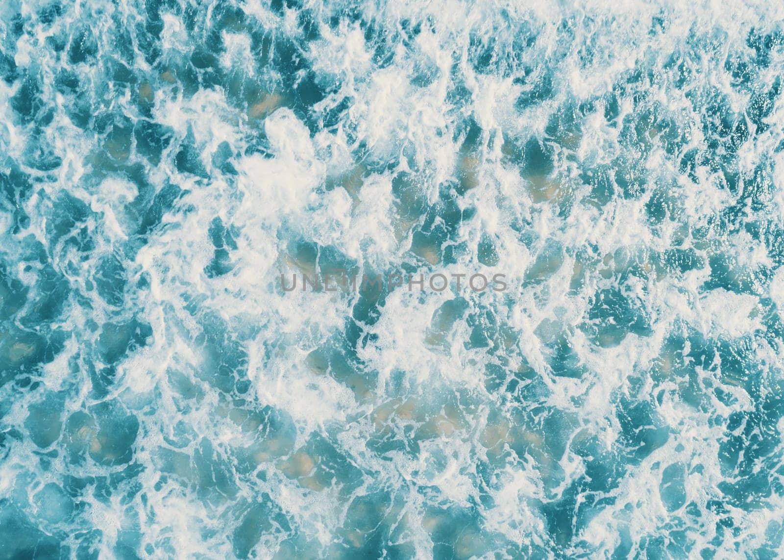 Aerial view of white foam on the surface of the blue sea.