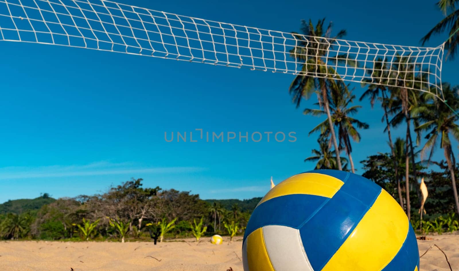 Low angle shot of game ball under sunlight and blue sky with volleyball net on the background