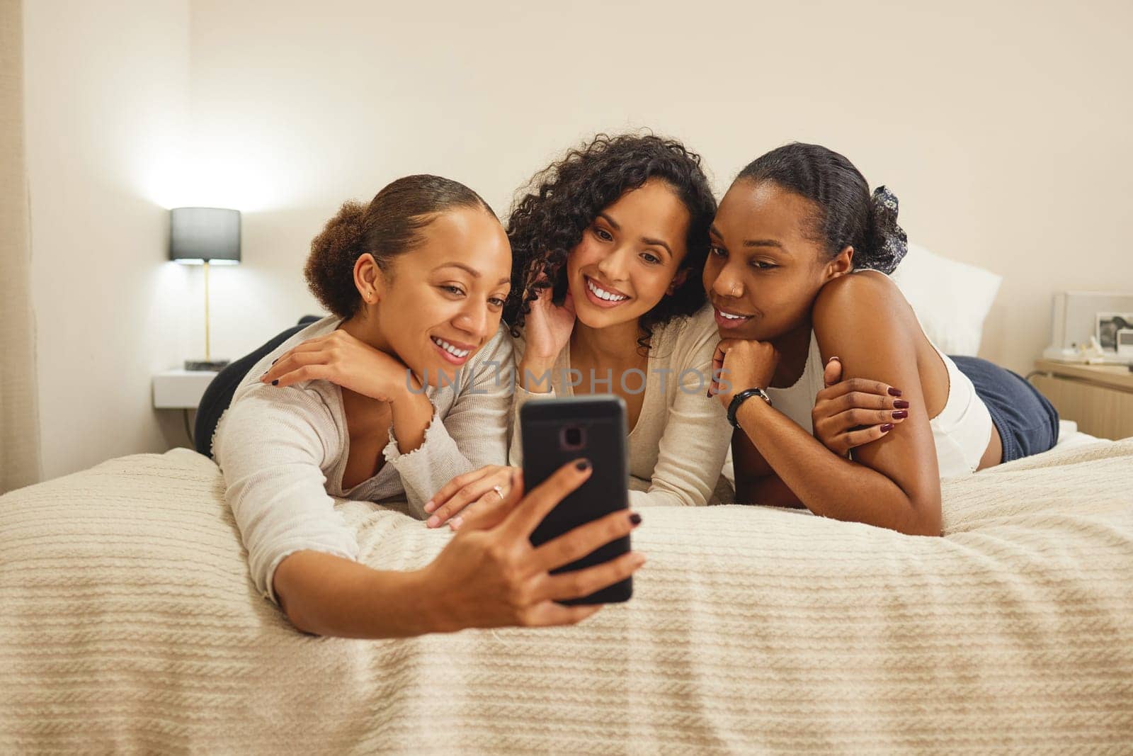 Women, selfie and friends in a home with profile picture, social media and smile at sleepover. Mobile, bonding and sister love in a bedroom with group, care and memories on a bed with digital app by YuriArcurs