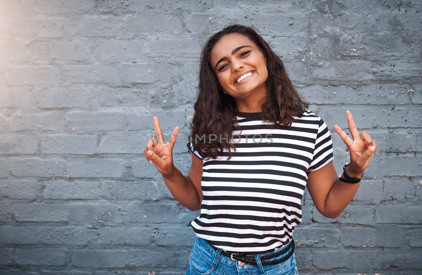 Brick, wall and peace sign for girl, smile and hands for gesture, outdoor and break for weekend. Proud, excited and student on holiday, morning and happiness on face, model and city of New York.