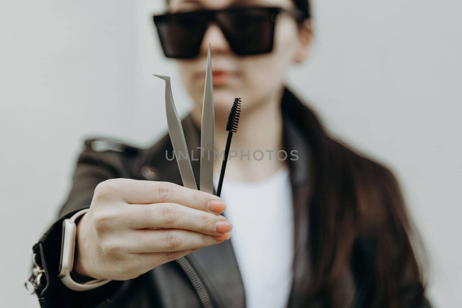 The girl shows tweezers and a brush for eyelash extensions. by Nataliya